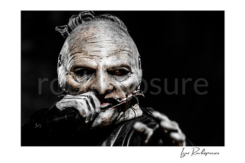 Horizontal color image of Corey Taylor of Slipknot in a tight masked close-up holding a handheld microphone and reaching toward the crowd