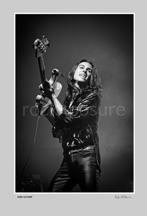 Vertical black and white image of Greta Van Fleet bassist Sam Kiszka performing live on stage