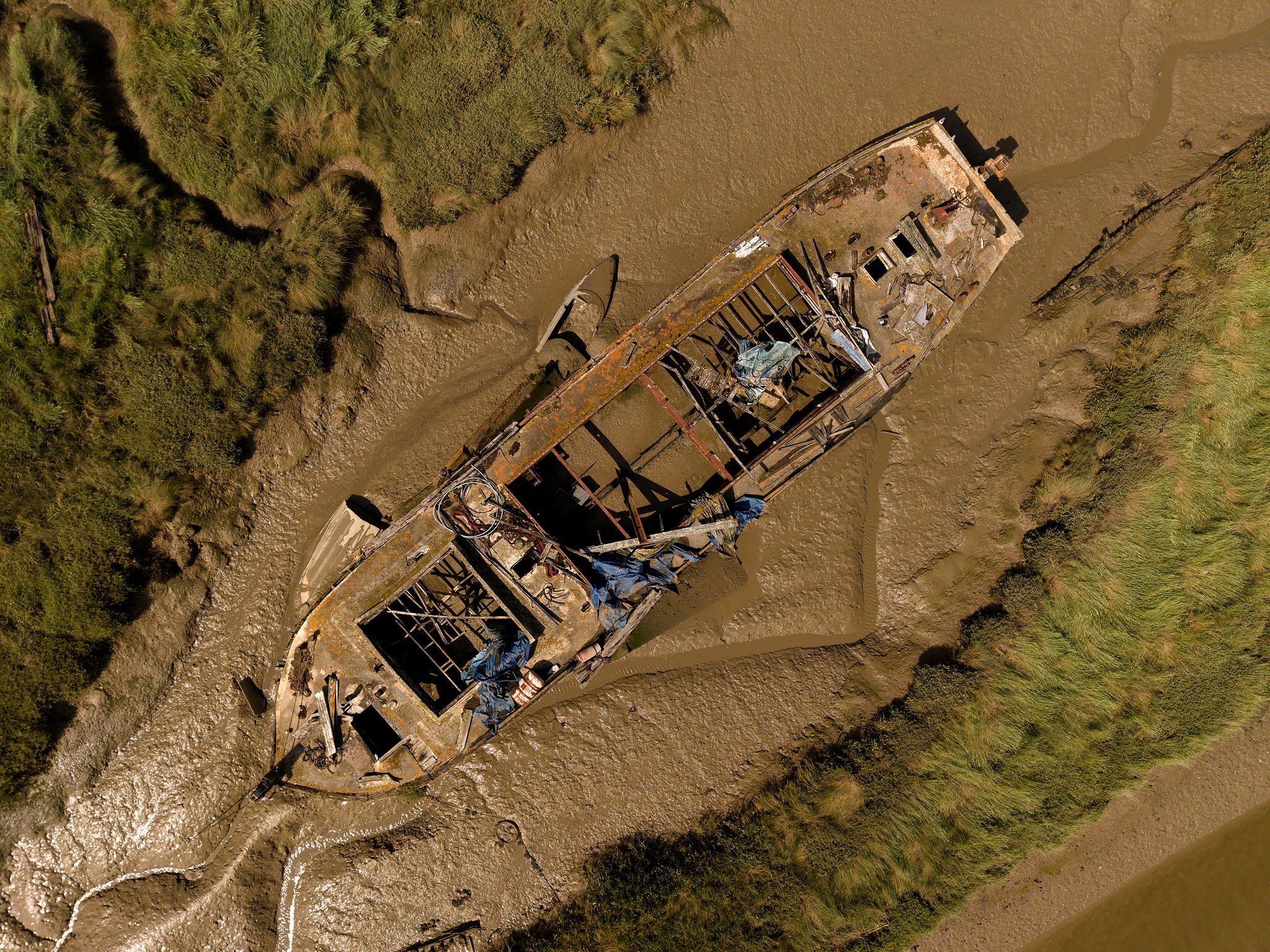 Aerial photograph of an abandoned boat wreck in the tidal mudflats of East Haven Creek, Benfleet, Essex, surrounded by saltmarsh and winding creeks.