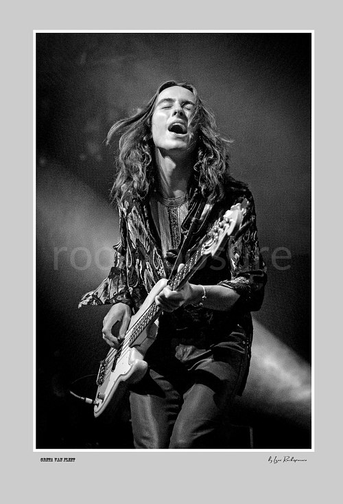 Vertical black and white image of Greta Van Fleet bassist Sam Kiszka performing live with his bass guitar