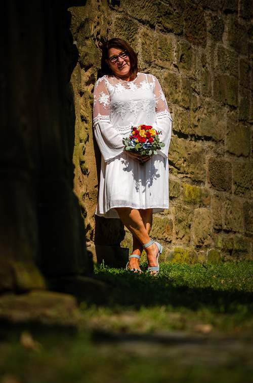 Braut im weißen Kleid mit Brautstrauß steht in einem Durchgang der Burgruine Weibertreu