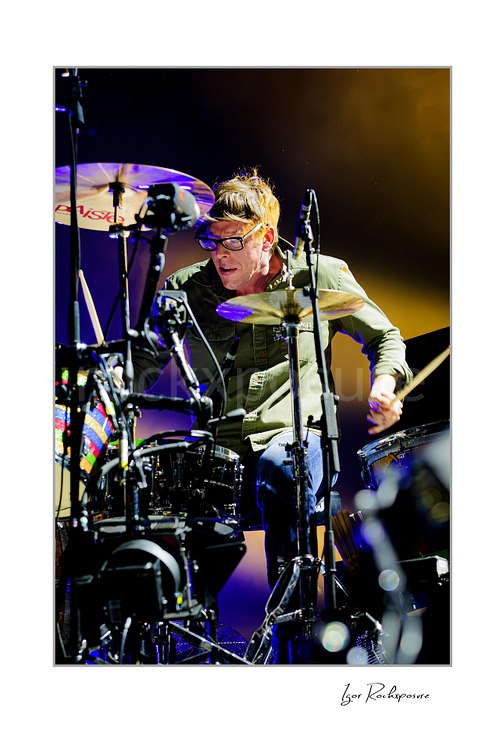 Vertical color image of Patrick Carney of The Black Keys playing drums under warm golden stage lighting