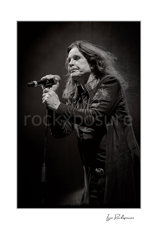 Ozzy Osbourne of Black Sabbath singing into a microphone captured in a dramatic black and white portrait during a live performance