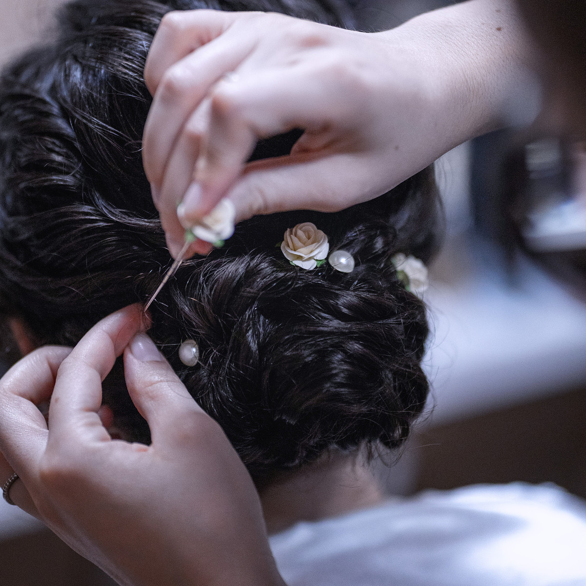 a hair stylist adding pink flower pins to a braided bun.