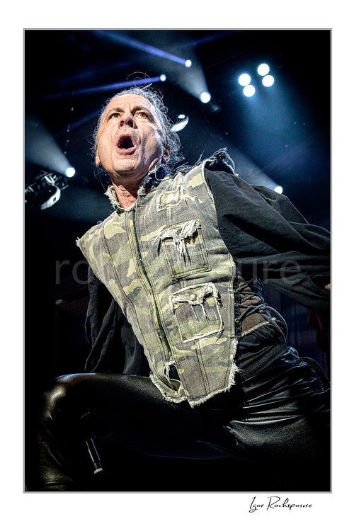 Vertical color close-up image of Bruce Dickinson of Iron Maiden performing live on stage under bright concert lights.