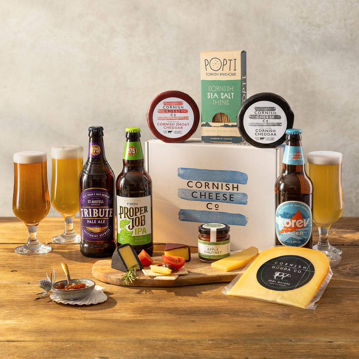 A Cornish Cheese co hamper with beer photographed on a plain textured studio background