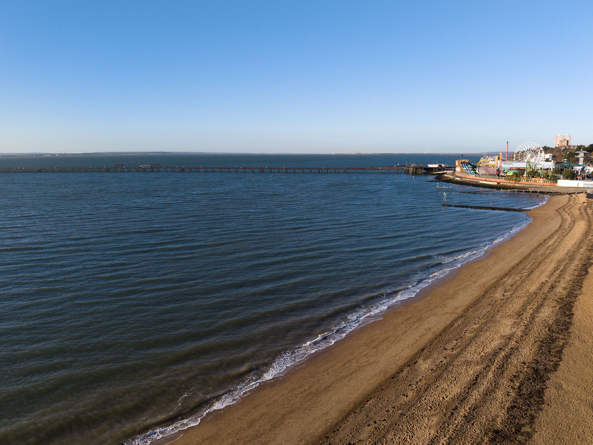 Aerial photograph of  a calm coastline with gentle waves, sandy beach, and Southend Pier extending into the sea during soft evening light
