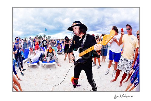 Horizontal color image of Randy Hansen playing guitar on a beach surrounded by fans during an outdoor performance