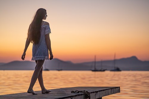 Femme marchant sur un ponton devant un ciel orangé au coucher du soleil à Hyères