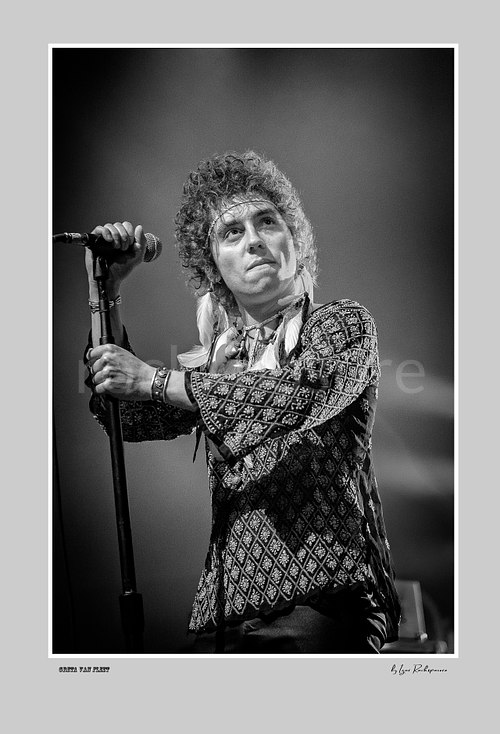 Vertical black and white image of Greta Van Fleet singer Josh Kiszka holding a microphone stand during a live performance