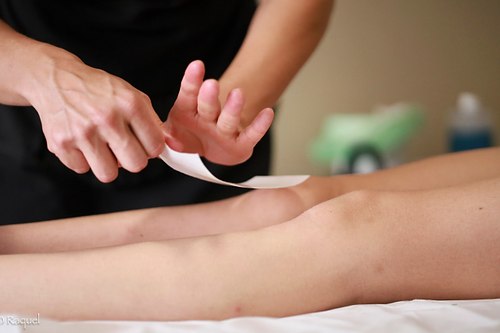 Esthéticienne réalisant une épilation à la cire avec des bandes sur la jambe d’une cliente.
