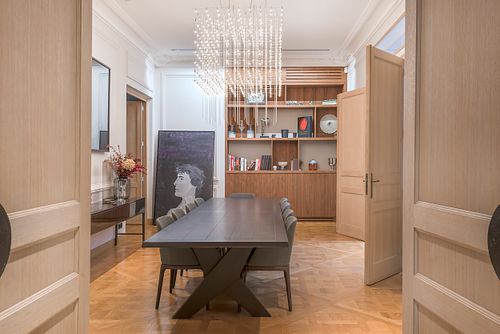 Salle à manger haussmannienne sur les Champs-Élysées avec table noire, chaises grises et lustre cascade en cristal. Photographie d’architecture intérieure par Nicolas Karadimos.