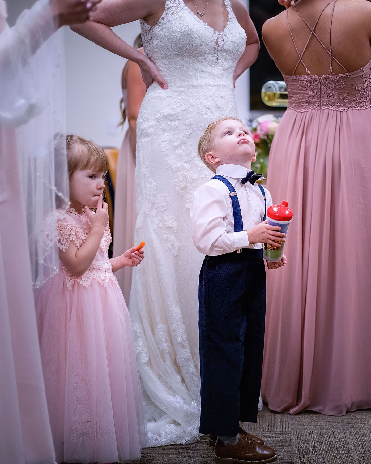 ring bearer looking up with bride standing behind him, he is holding a sippy cup