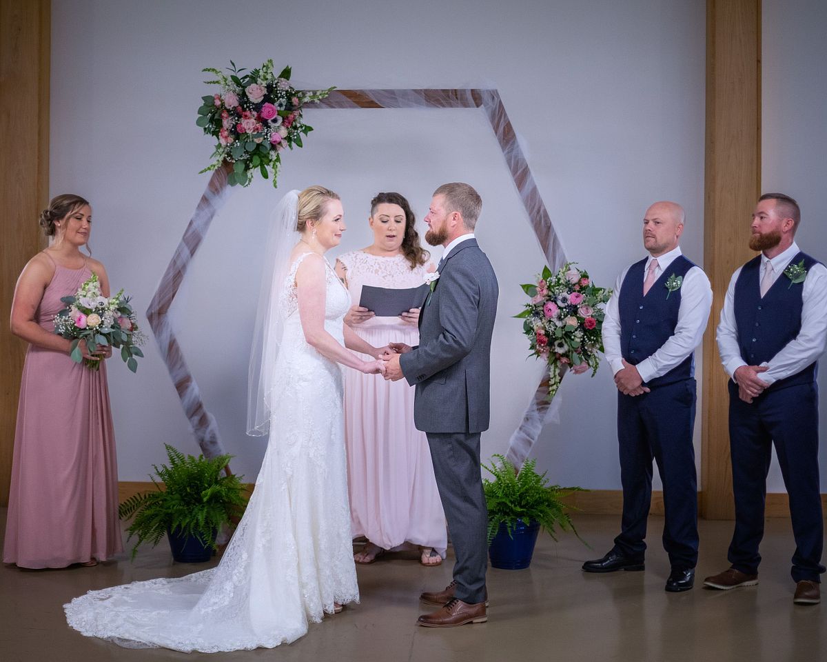 couple saying their wedding vows surrounded by the wedding party while officiant is speaking