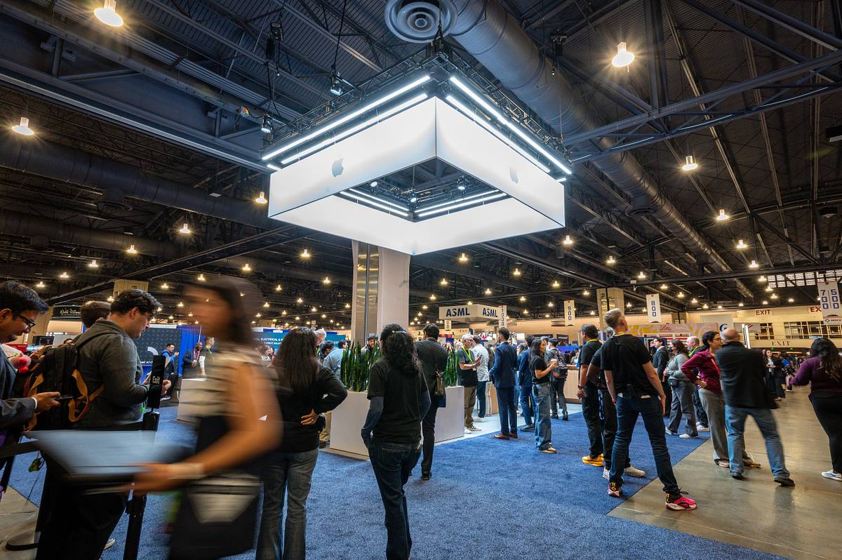 A motion-blurred attendee moves past the illuminated Apple exhibit as professionals gather and connect on the SHPE 2025 convention floor.