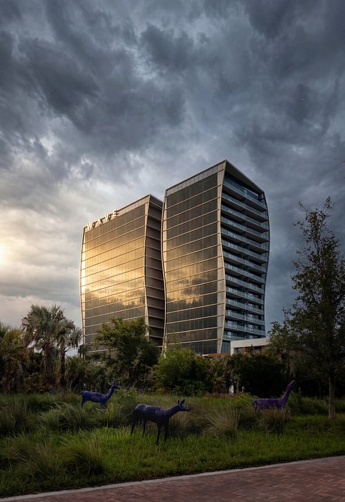 Dusk exterior of the Lake Nona Wave Hotel in Orlando, FL, designed by Arquitectonica, featuring foreground deer sculptures under an overcast sky.