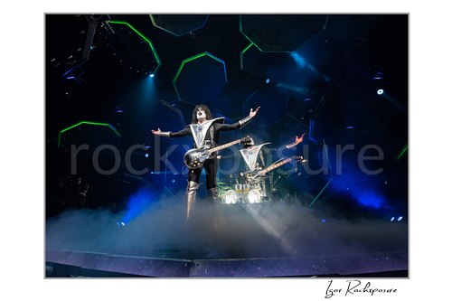 Tommy Thayer of KISS performing in a wide guitar stance under blue arena stage lighting with illuminated stage arches behind him