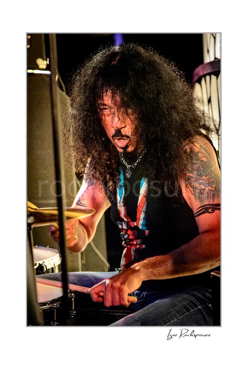 Vertical color image of Frankie Banali playing drums onstage in a tight live performance close-up with intense expression