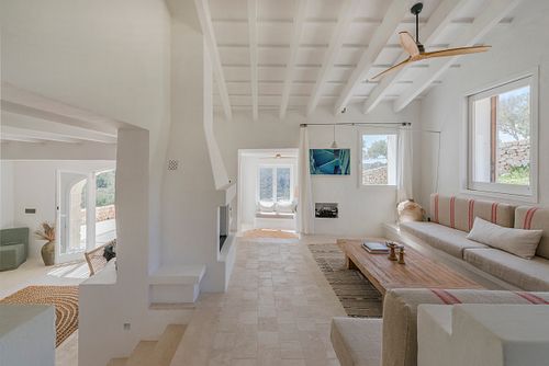 Salon lumineux avec cheminée, banquettes intégrées et grande ouverture sur l’extérieur dans la finca Son Fonoll à Minorque. Photographie par Nicolas Karadimos.