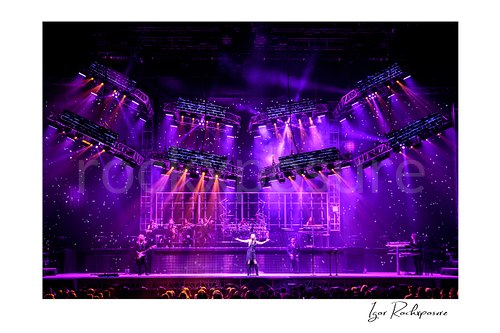 Horizontal color image of Trans Siberian Orchestra performing on stage beneath purple lighting with the full band and orchestra visible