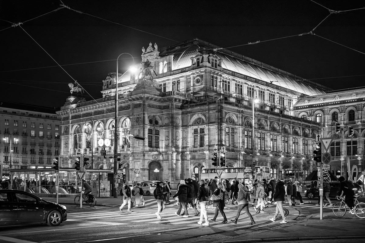 Schwarz-Weiß-Fotografie der Wiener Staatsoper bei Nacht während Menschen über die Straße eilen
