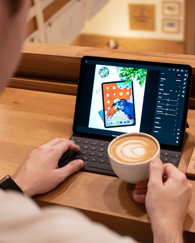 Person, die mit einem Kaffee in der Hand ein Foto auf einem Tablet bearbeitet