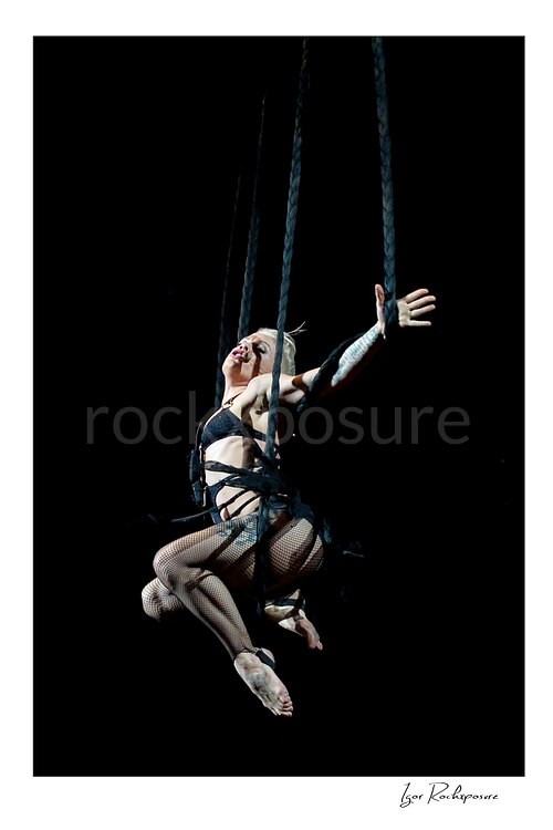Vertical color image of Pink suspended high above the stage on ropes with one arm outstretched during a dramatic live performance