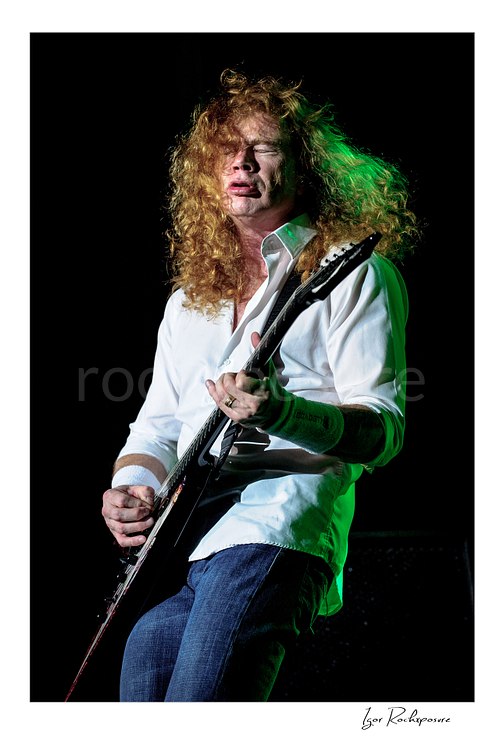 Vertical color image of Dave Mustaine of Megadeth playing guitar on stage with curly red hair and green stage light