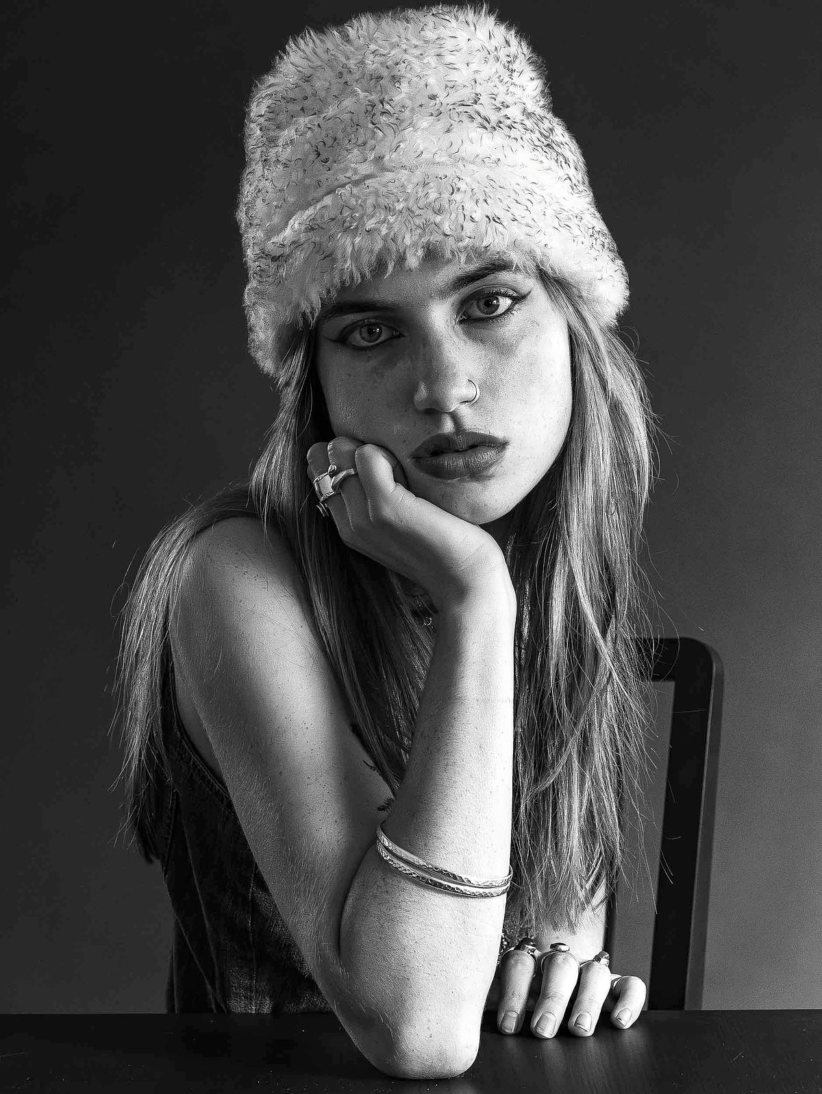 Headshot portrait of a girl leaning her face into her hand and her elbow rests on a table.