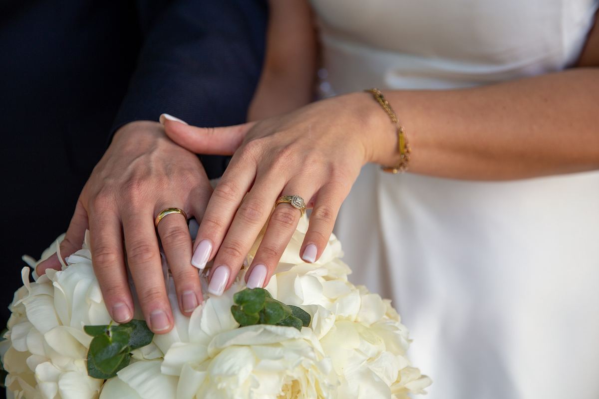 Close-up of bride and groom showing their wedding rings over a white bridal bouquet
