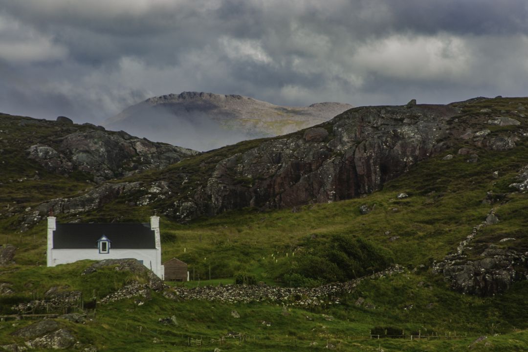 A small white house surrounded by rugged hills near Oldshoremore, Scotland.