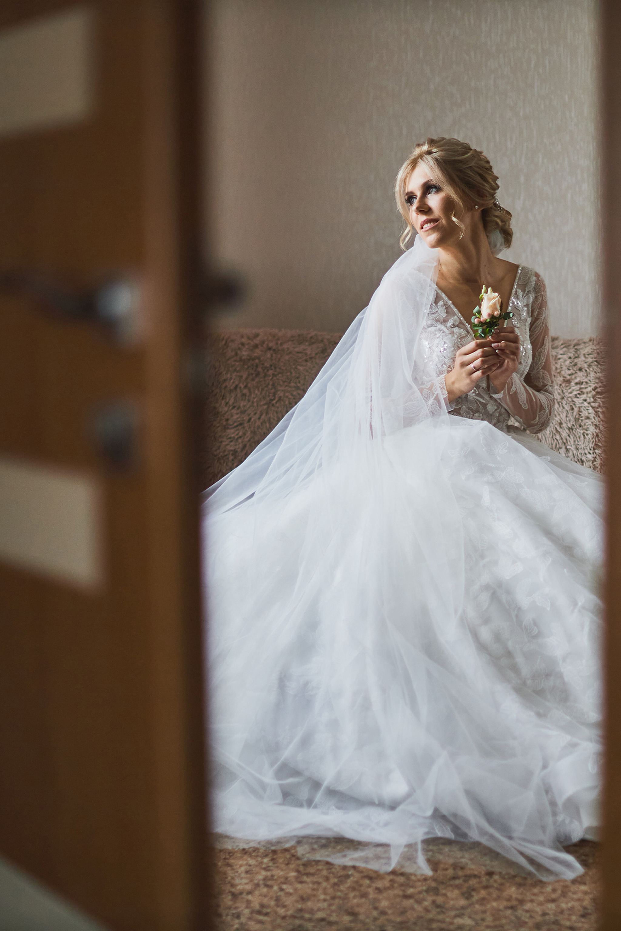 Bride seated in soft window light holding a delicate rose