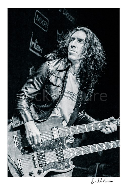Vertical black and white image of Brent Woods playing double-neck guitar on stage in a tight performance shot