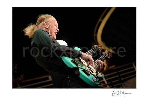 Horizontal color image of Billy Sheehan playing his double-neck bass in an energetic side-stage performance shot
