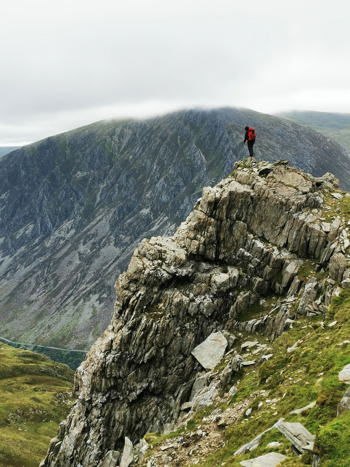 Hiker standing on a rocky cliff overlooking the mountains of Wales during a multi-day hiking journey.