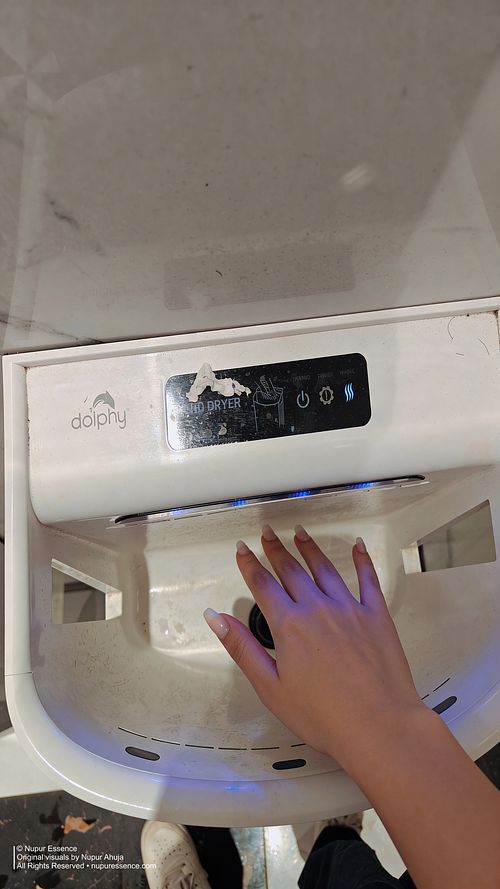 Close-up lifestyle detail featuring Nupur Ahuja hand under an automatic dryer with manicured nails, published through Nupur Essence