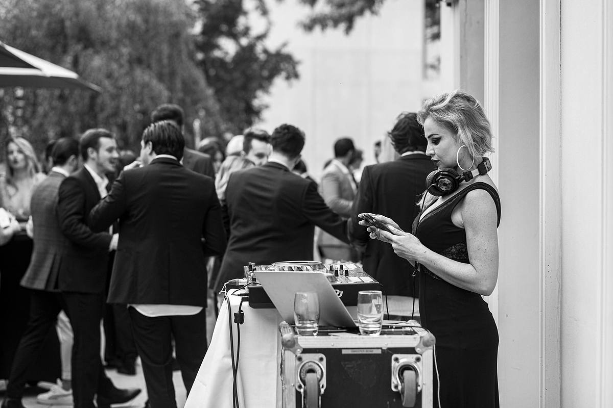 Dans une atmosph&egrave;re de convivialit&eacute;, une DJ &eacute;l&eacute;gante s&eacute;lectionne les prochains hits sur son smartphone, tandis que les invit&eacute;s en arri&egrave;re-plan &eacute;changent des anecdotes, captur&eacute;e par Sebastien CLAVEL Photographe mariage Lyon