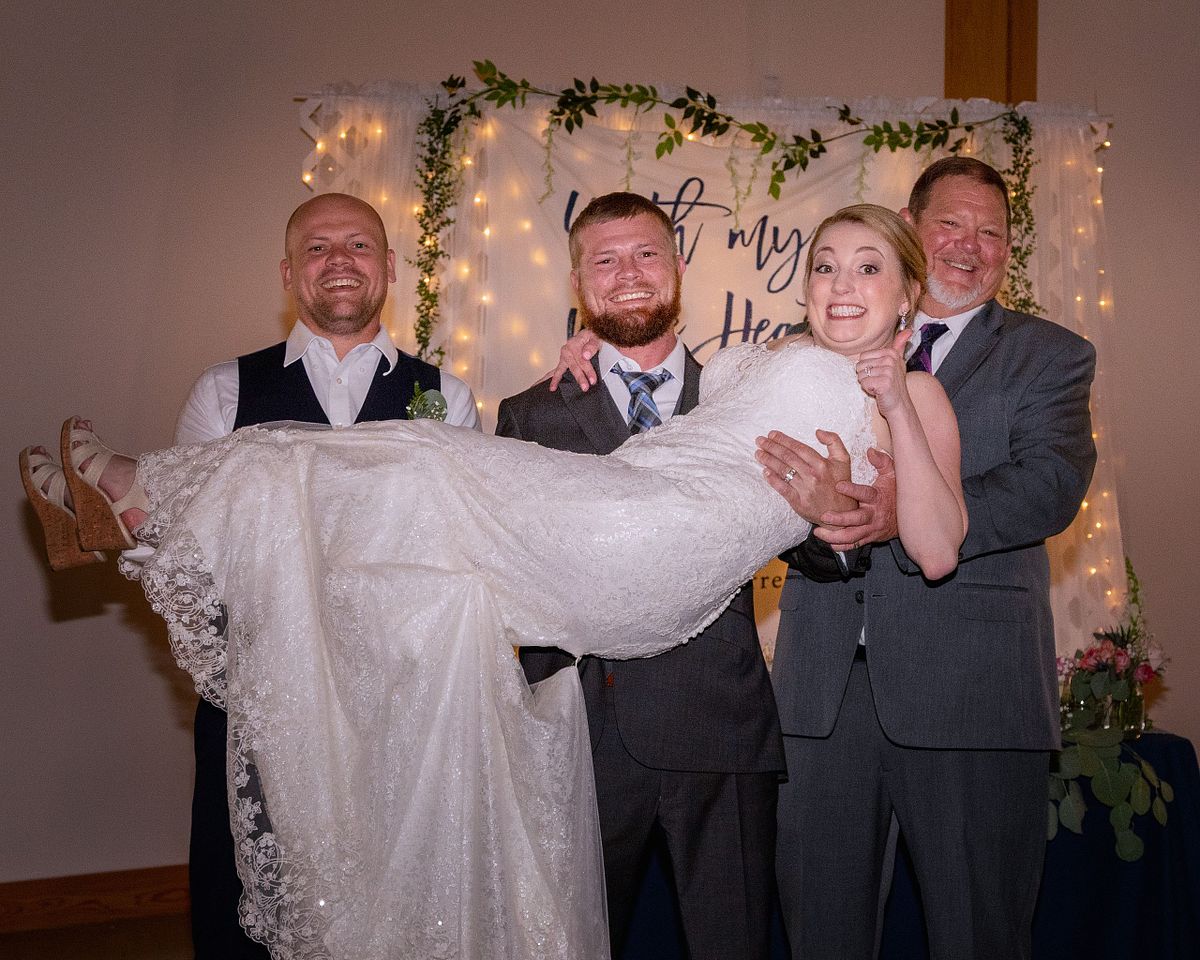 groom and two groomsmen lifting the bride up, the bride is looking worried