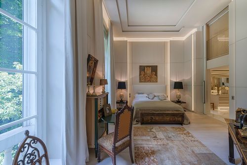 Chambre à coucher haussmannienne à Saint-Germain-des-Prés avec lit central, lumière naturelle provenant des grandes fenêtres et mobilier élégant. Photographie d'architecture intérieure par Nicolas Karadimos.