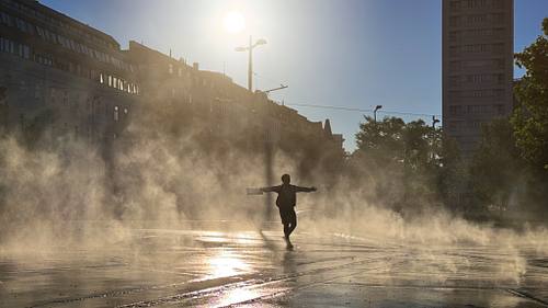 Silhouette eines Kindes mit ausgestreckten Armen beim Tanzen im dichten, von der Sonne hinterleuchteten Wassernebel des Wasserspiels am Wiener Praterstern.