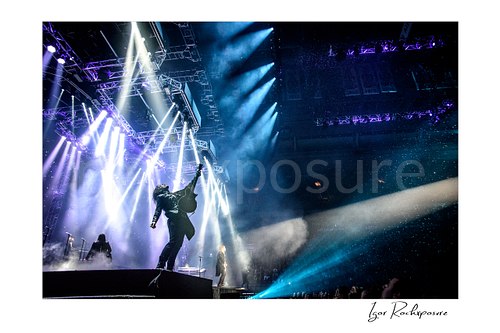 Horizontal color image of Trans Siberian Orchestra guitarist in silhouette on stage beneath dramatic white and blue concert lighting