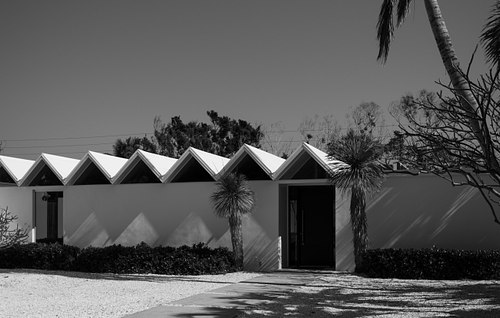 Low-angle black and white architectural photograph capturing the striking saw-toothed roof structure and minimalist design of the historic Zigzag House in Sarasota, Florida.