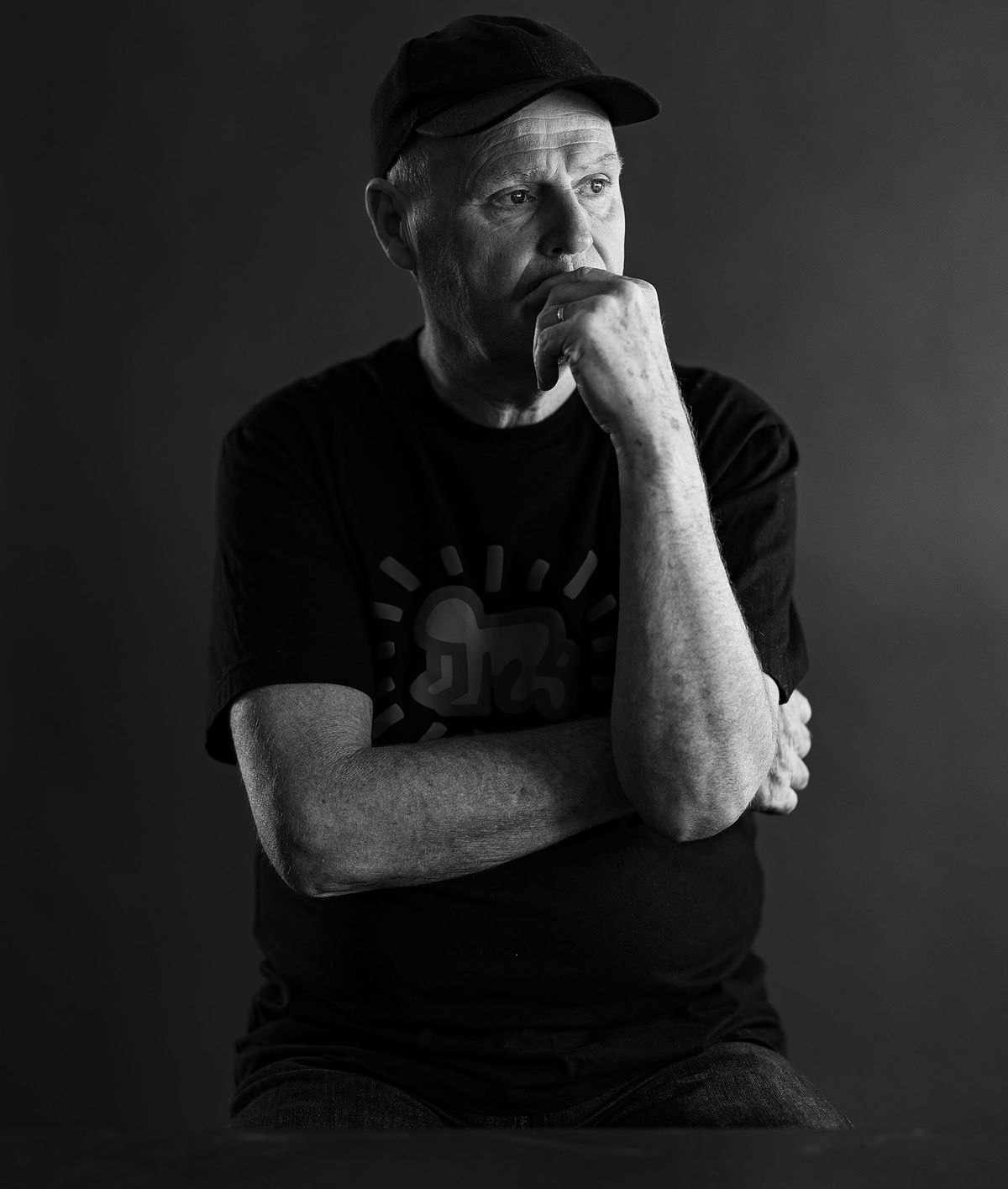 Portrait of artist and teacher Stuart Murdoch. He wears a black t-shirt. Dark grey background.