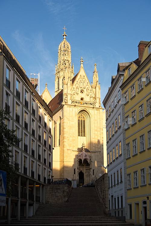 Maria am Gestade in Wien im goldenen Abendlicht, gesehen über die Freitreppe zwischen historischen Häuserzeilen der Wiener Innenstadt.