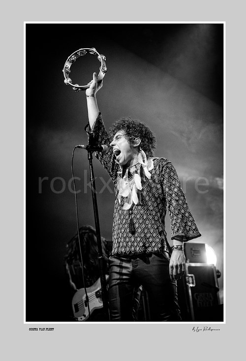 Vertical black and white image of Greta Van Fleet singer Josh Kiszka holding a tambourine above his head during a live performance