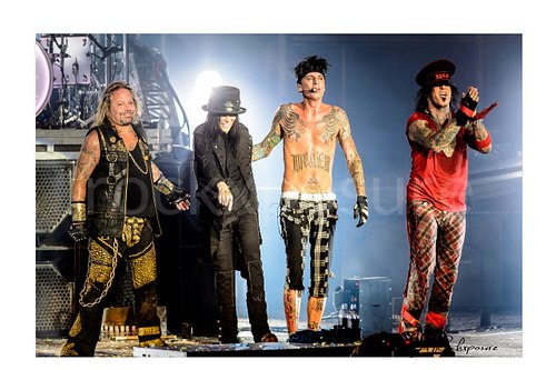 Horizontal color image of Mötley Crüe performing live on stage with Vince Neil, Mick Mars, Tommy Lee, and Nikki Sixx under bright concert lighting
