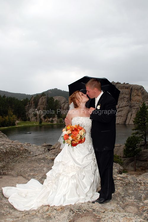 A bride and groom under a black umbrella standing on the rocks at Sylvan Lake.