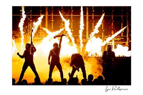 Horizontal color image of Trans Siberian Orchestra performing in silhouette with guitars, microphone, flames, and stage pyrotechnics