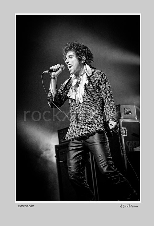Vertical black and white image of Greta Van Fleet singer Josh Kiszka singing into a microphone during a live performance