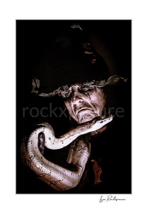 Vertical color image of Alice Cooper holding a snake in a dark theatrical close-up portrait